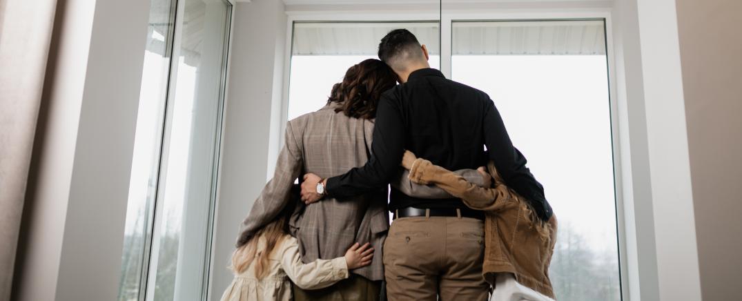 Familia abrazada de espaldas, unida frente a una ventana, simbolizando apoyo y contención emocional
