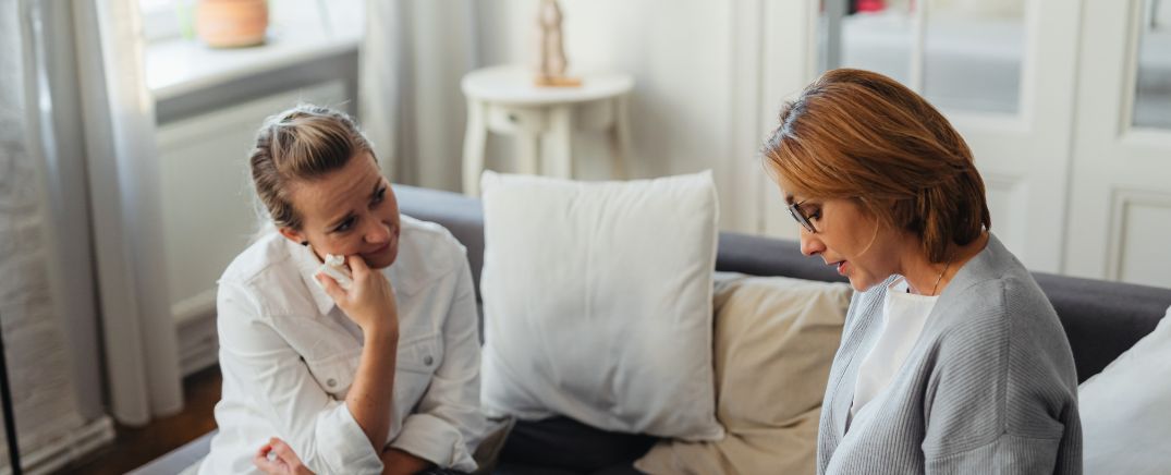 Dos mujeres sentadas en un sofá manteniendo una conversación emocional, representando un diálogo familiar sobre un problema con el alcohol.