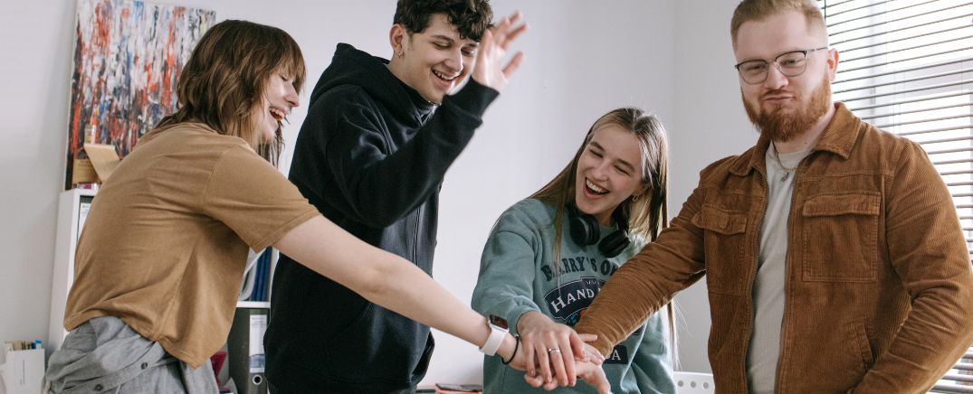 Grupo de jóvenes uniéndose con las manos en señal de apoyo, confianza y acompañamiento para superar una adicción.